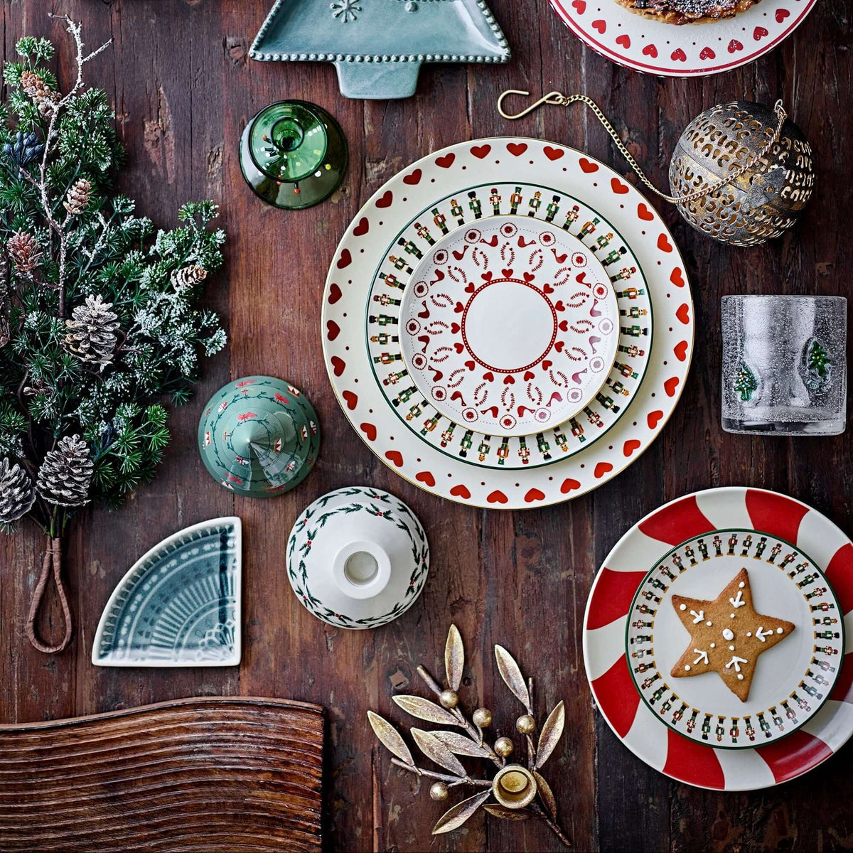 Decorative table setting with plates, ornaments, and a tree-shaped candle holder on a wooden surface.