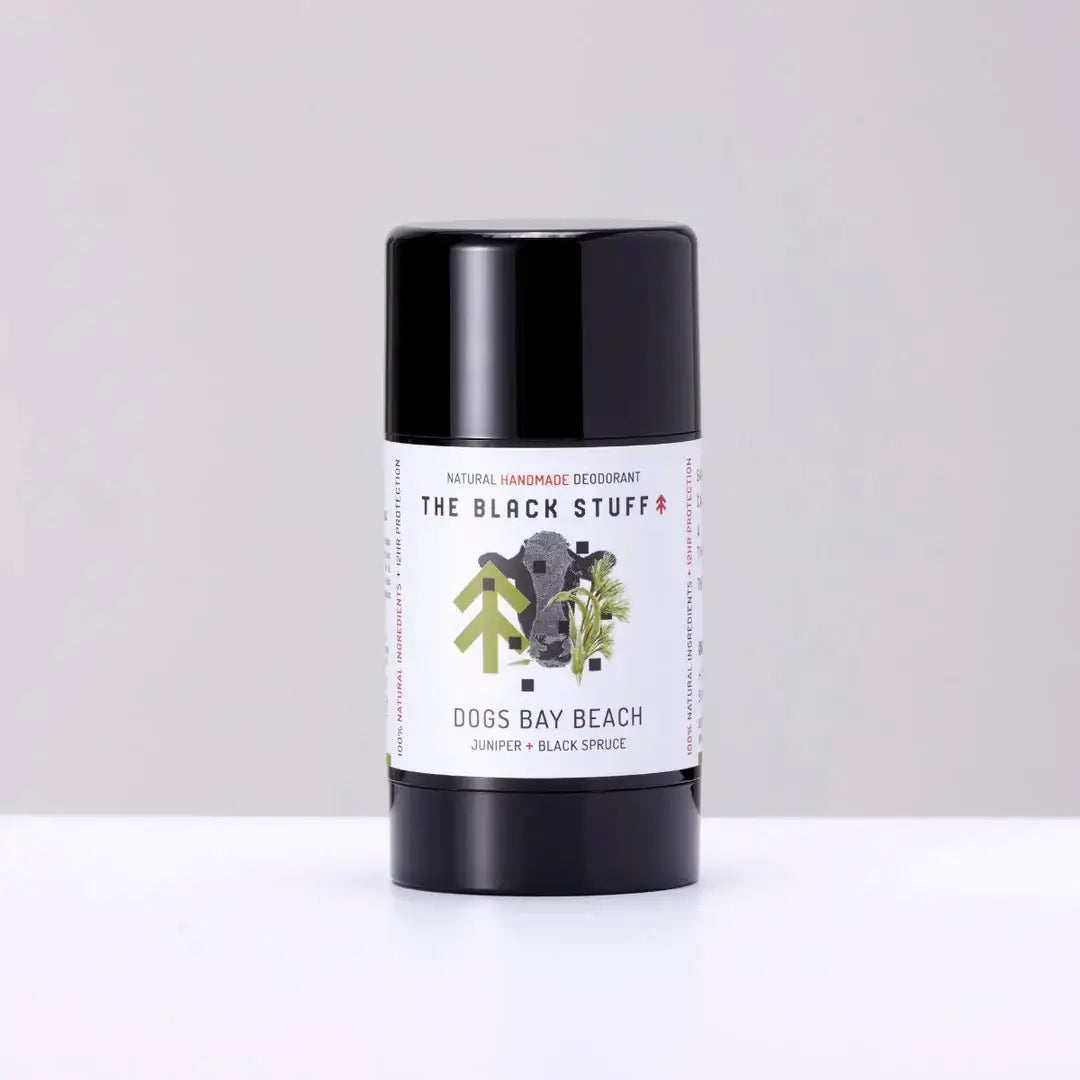 A stick deodorant with a black lid and a label that has 'The Black Stuff' and 'Dogs Bay Beach' written on it, indicating it is a natural deodorant for men.