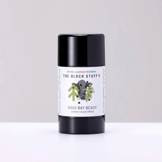 A stick deodorant with a black lid and a label that has 'The Black Stuff' and 'Dogs Bay Beach' written on it, indicating it is a natural deodorant for men.