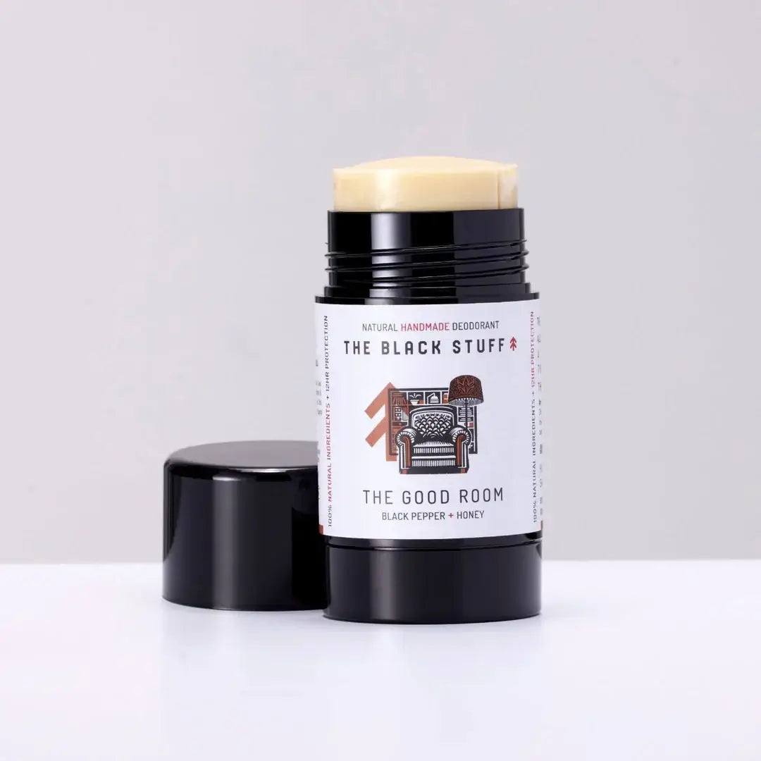A stick deodorant labeled 'The Good Room' by The Black Stuff, with a black cap and a label that has text and an illustration of a chair.