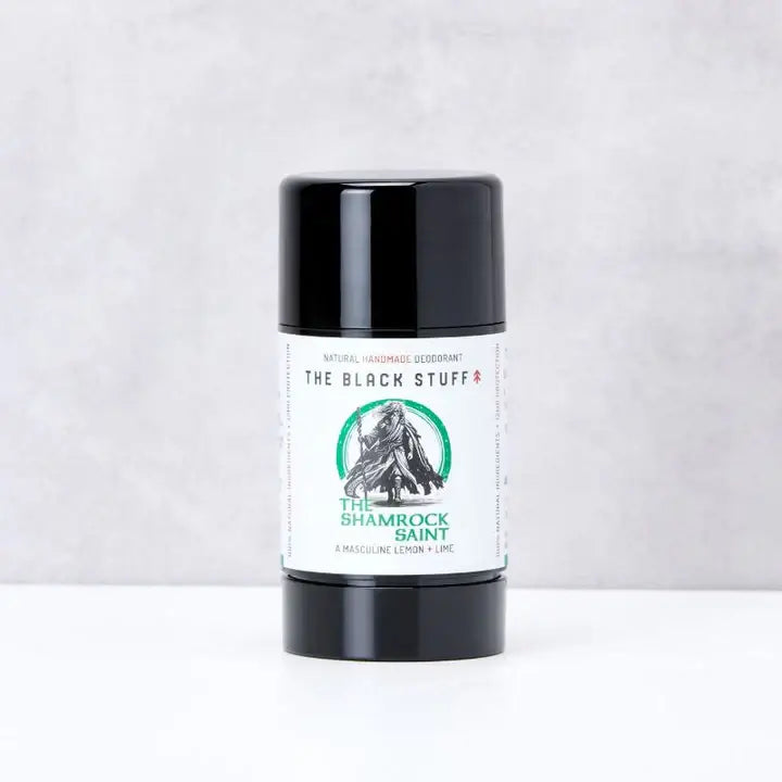 A stick of natural deodorant labeled 'The Shamrock Saint' by The Black Stuff, placed upright on a textured surface.