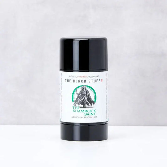 A stick of natural deodorant labeled 'The Shamrock Saint' by The Black Stuff, placed upright on a textured surface.