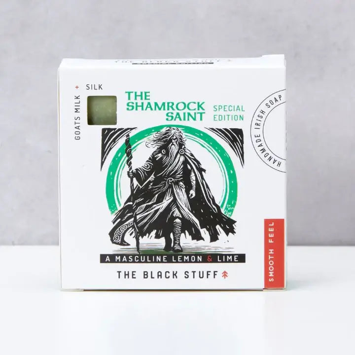 Packaging of 'The Shamrock Saint' natural soap by The Black Stuff featuring an illustration of a hooded figure holding a staff, with green accents and text indicating the product name and description.