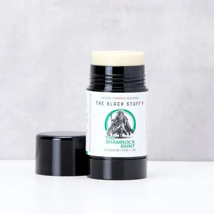 A stick of natural deodorant labeled 'The Shamrock Saint' by The Black Stuff, placed upright on a textured surface.