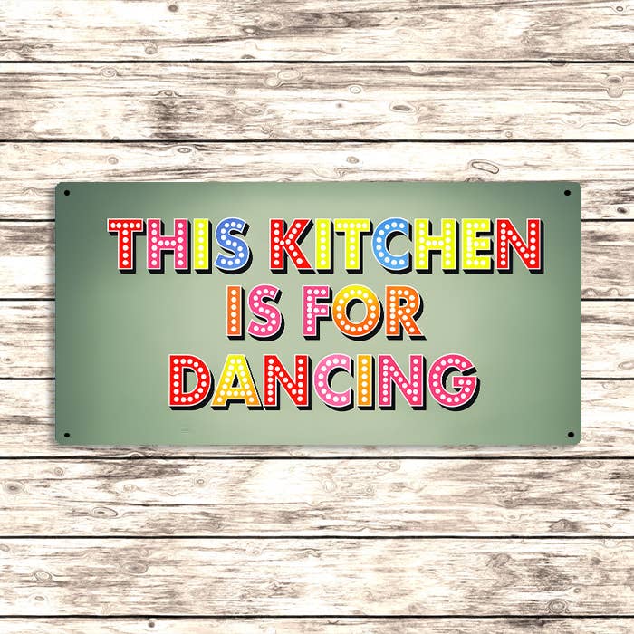Decorative sign with colorful text 'THIS KITCHEN IS FOR DANCING' on a wooden background