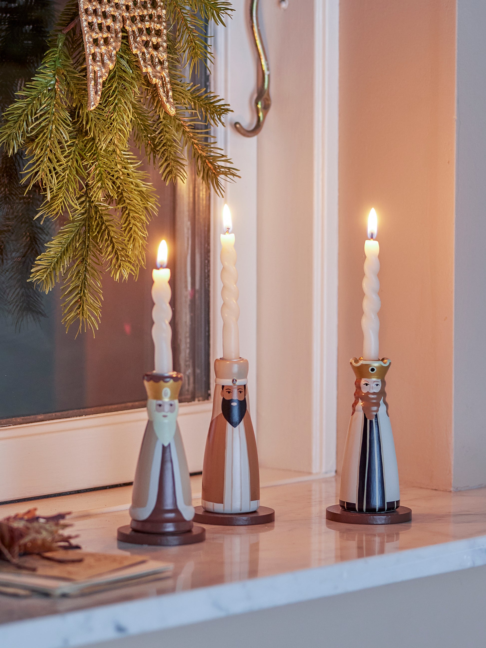 Three wise men painted candle holders with lit taper candles. Sitting on a windowsill