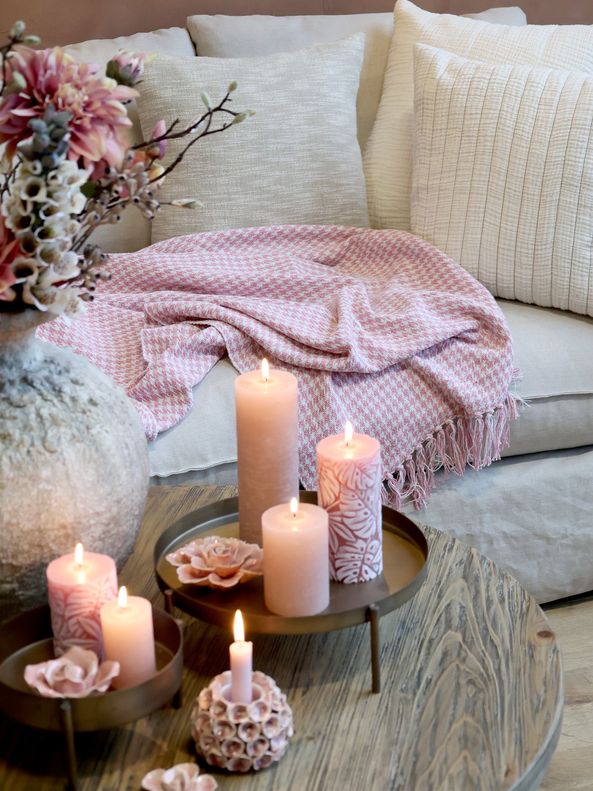 Candlelit scene with candles on a coffee table in front of a sofa with pink blanket and pillows.