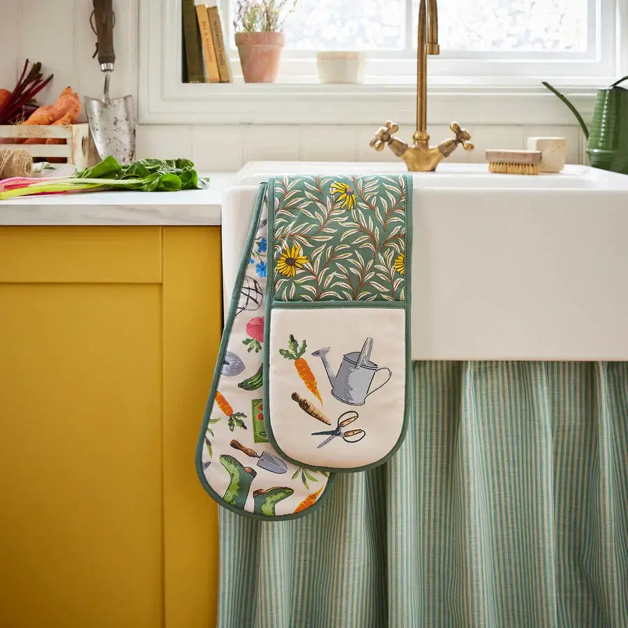 Colorful oven mitts with gardening-themed designs hanging on a kitchen cabinet.