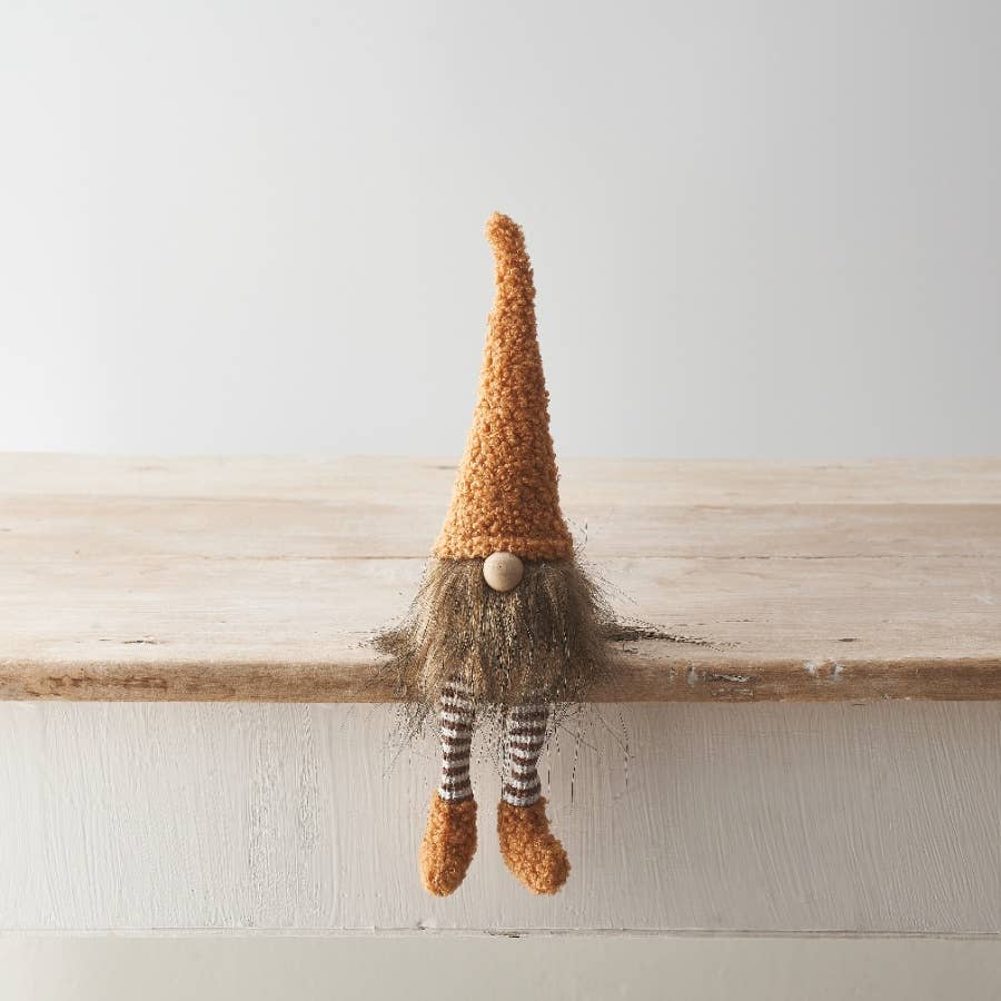 Knitted gnome with a tall hat and striped socks sitting on a wooden surface.
