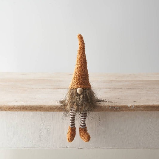 Knitted gnome with a tall hat and striped socks sitting on a wooden surface.
