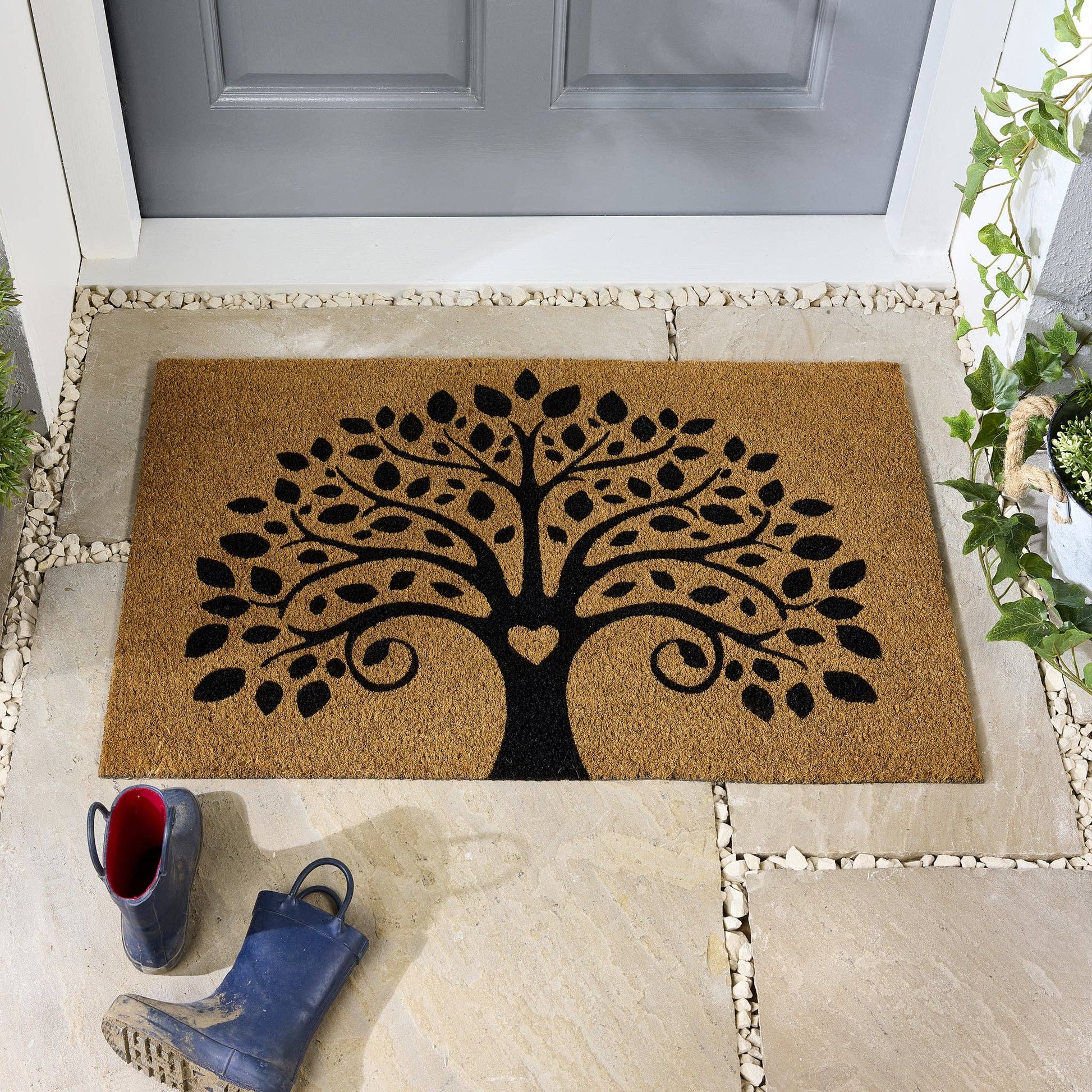Doormat with a tree design on a stone pathway in front of a door.