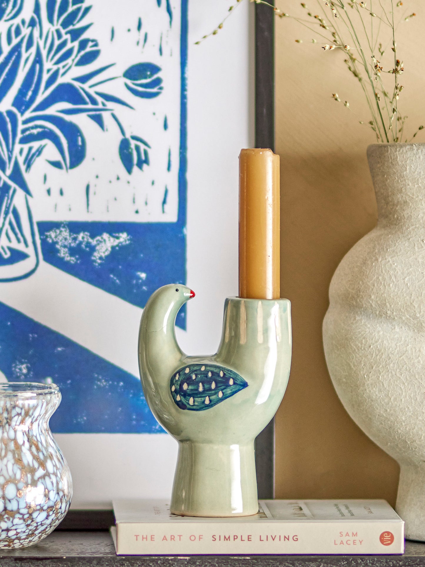 Decorative candle holder shaped like a bird, placed on a book with a blue and white abstract painting in the background.