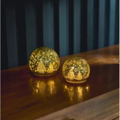 Two spherical gold-toned decorative lamps with a textured, glittery finish sitting on a dark wooden cabinet against a dark paneled wall.