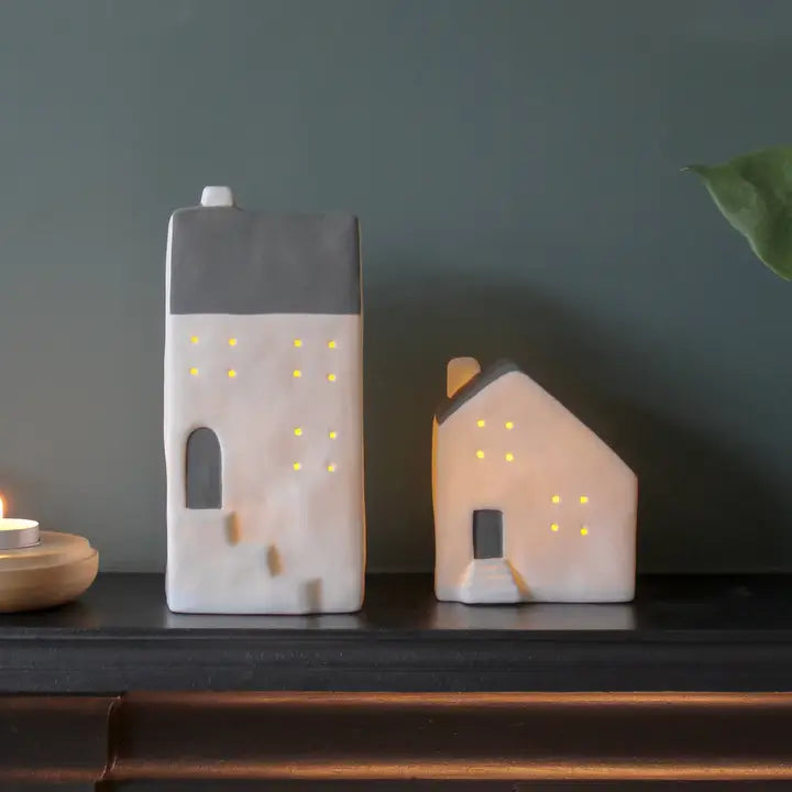 Two house-shaped ceramic lamps on a dark surface with a dark background