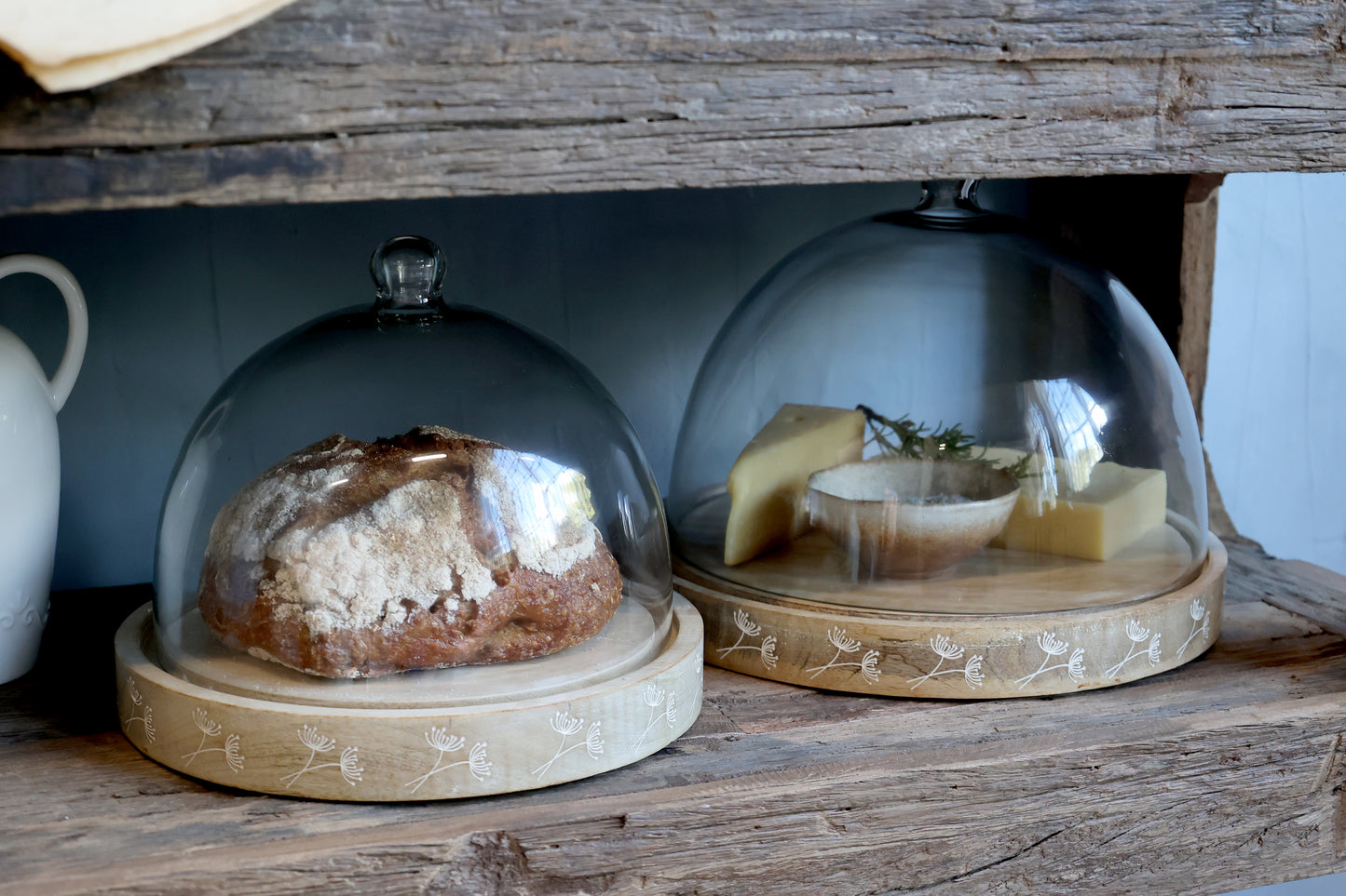 Two glass domes on wooden stands with food items inside, placed on a rustic wooden surface.