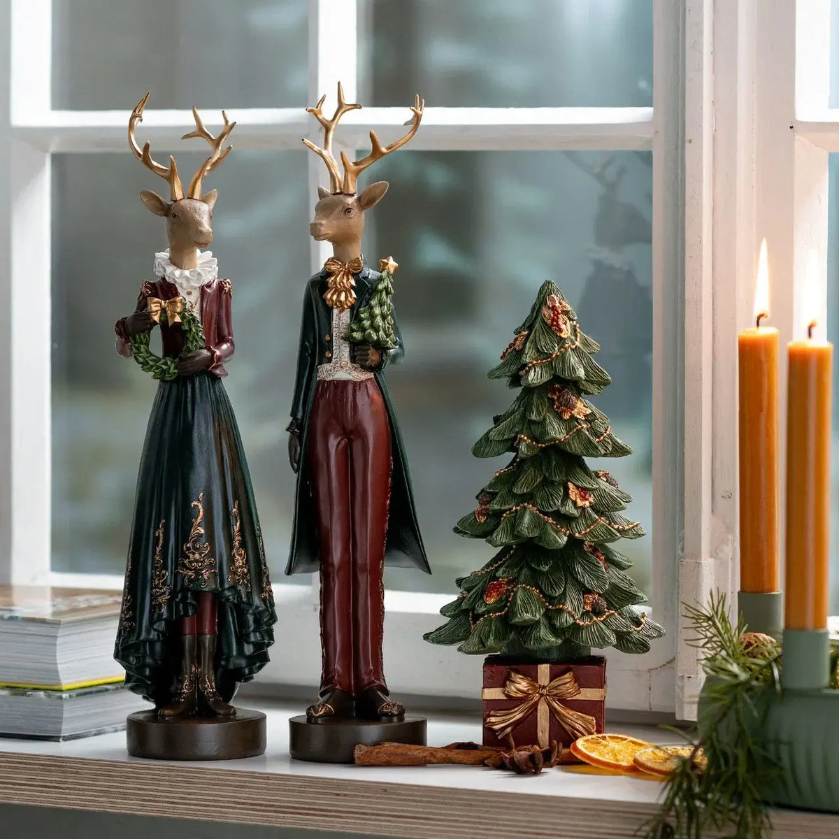Decorative deer statues and a small Christmas tree on a windowsill with candles.
