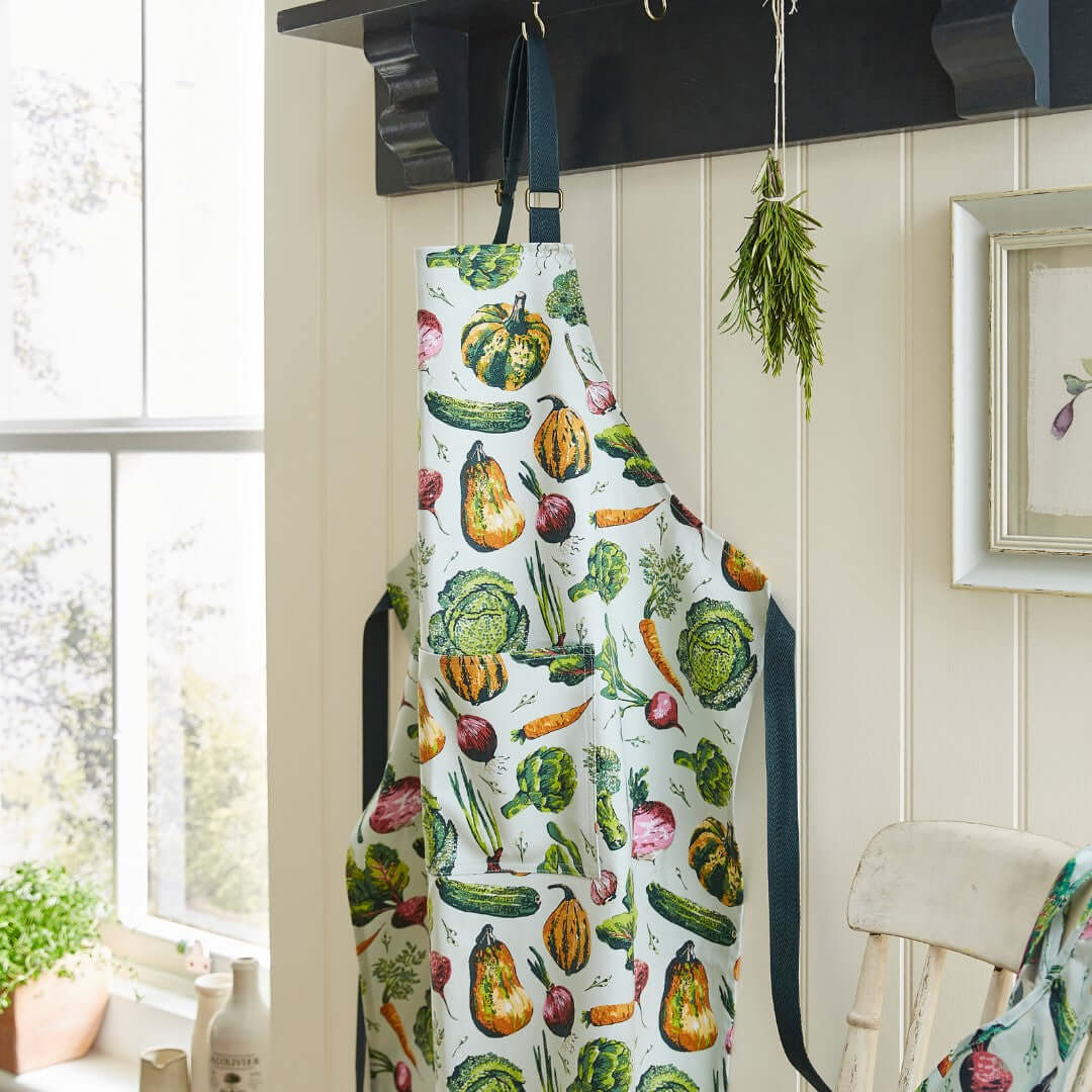 Colorful apron with vegetable pattern hanging on a hook in a kitchen.