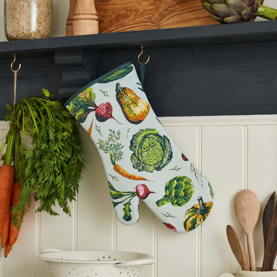 Decorative oven glove with vegetable pattern hanging on a shelf with kitchen items.