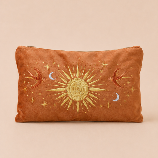A rectangular brown suede pouch with a celestial embroidered design featuring a central gold sun, red birds, blue crescent moons, and gold stars, set against a solid beige background.