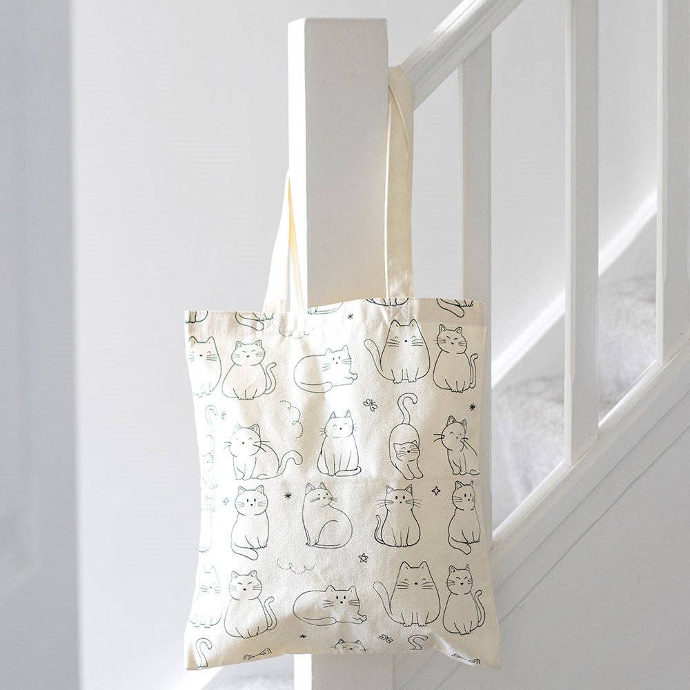 Tote bag with cat pattern hanging on a white railing.
