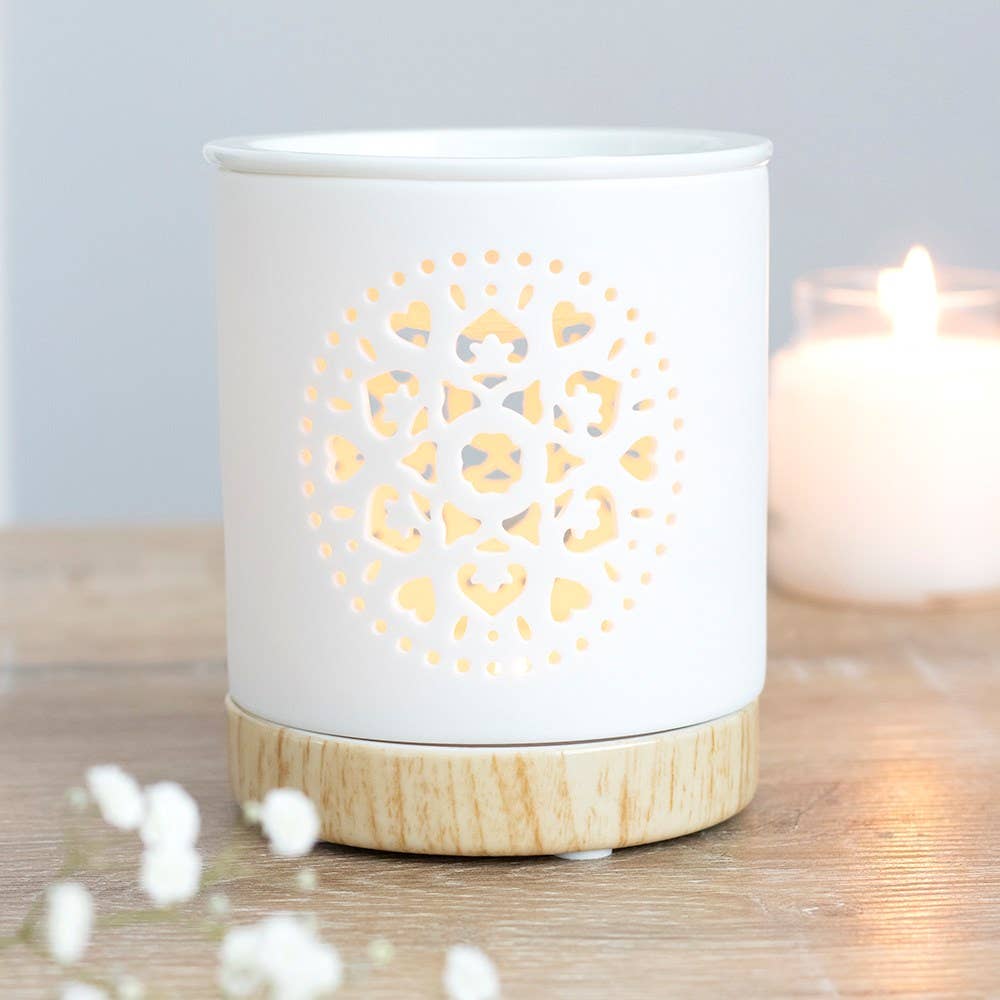 White ceramic diffuser with wooden base on a wooden surface, surrounded by white flowers.