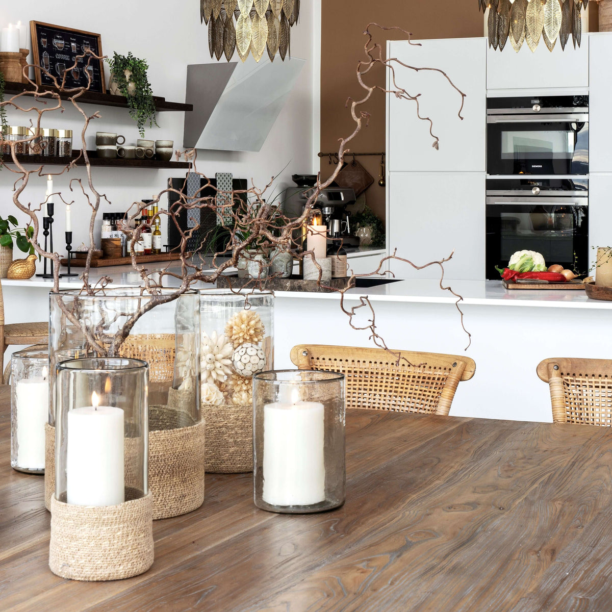 Decorative setup with candles and branches on a wooden table in a modern kitchen.