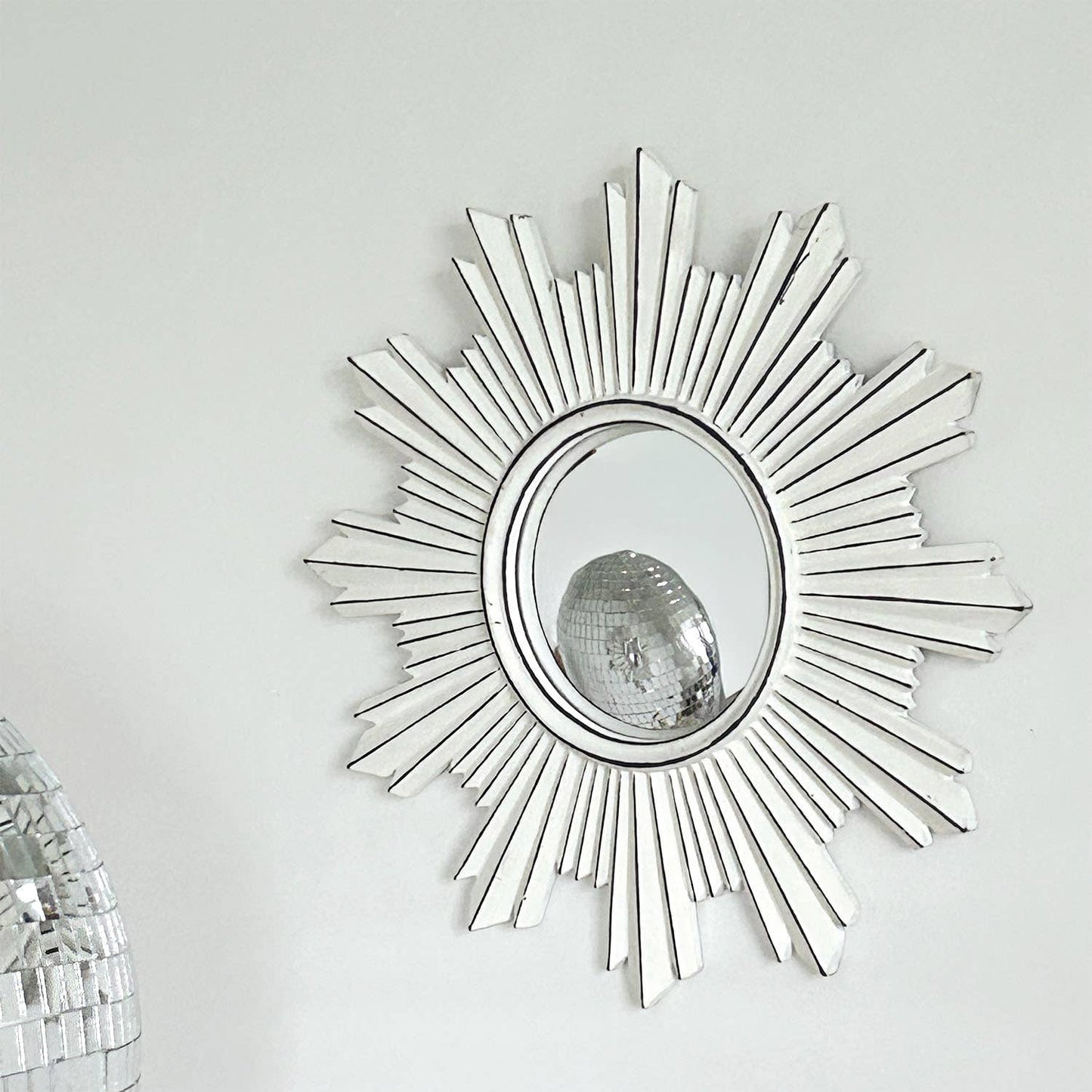 Decorative sunburst mirror with a disco ball on a white wall