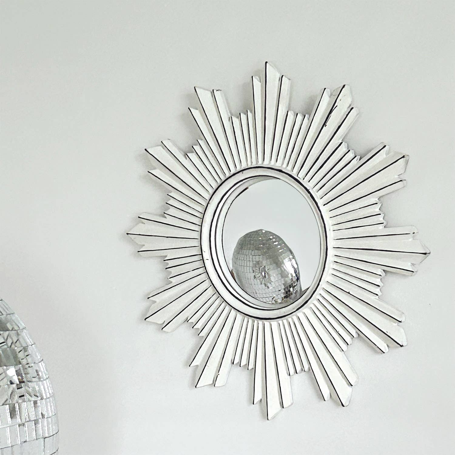 Decorative sunburst mirror with a disco ball on a white wall