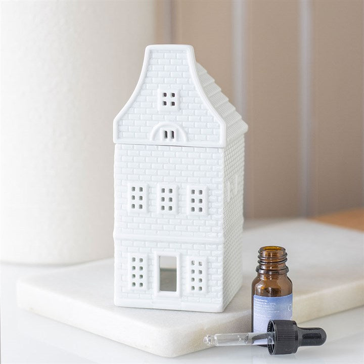 White house-shaped oil burner with a bottle and dropper on a white surface