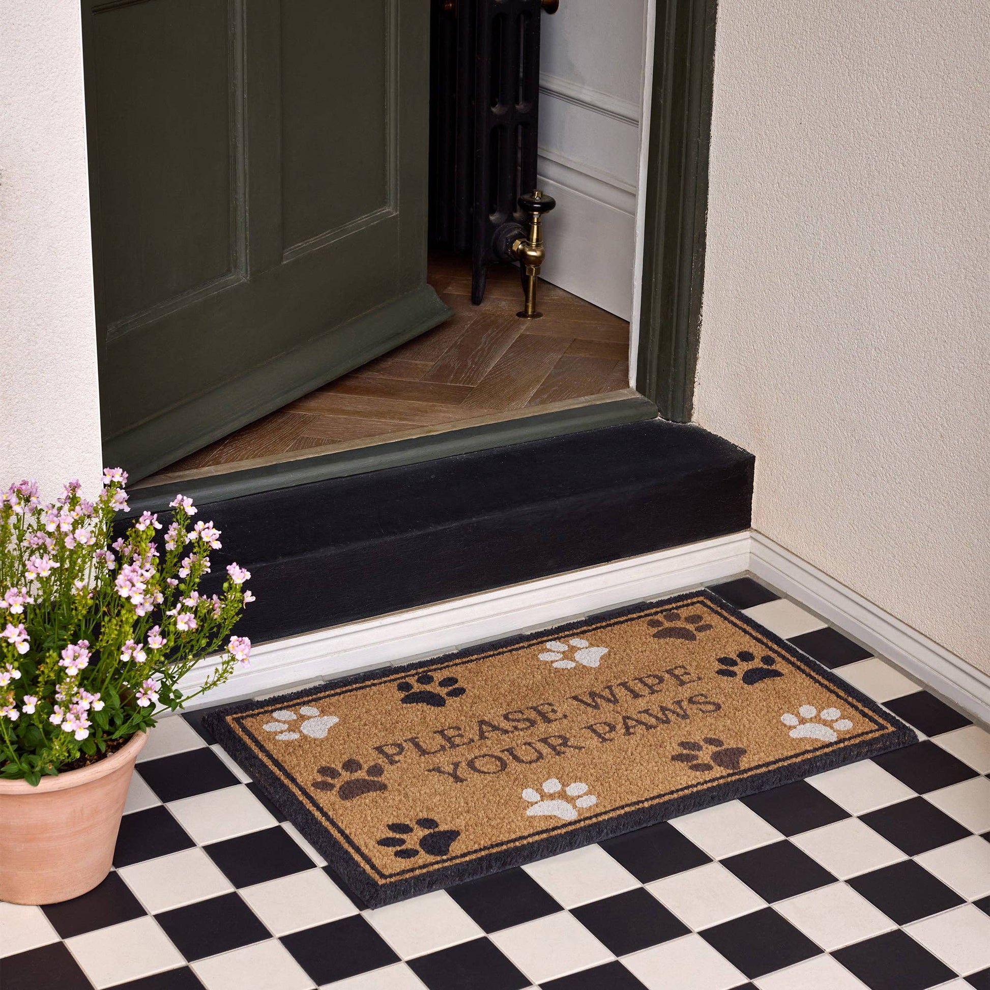 Doormat with paw prints and text on a checkered floor in front of a door.