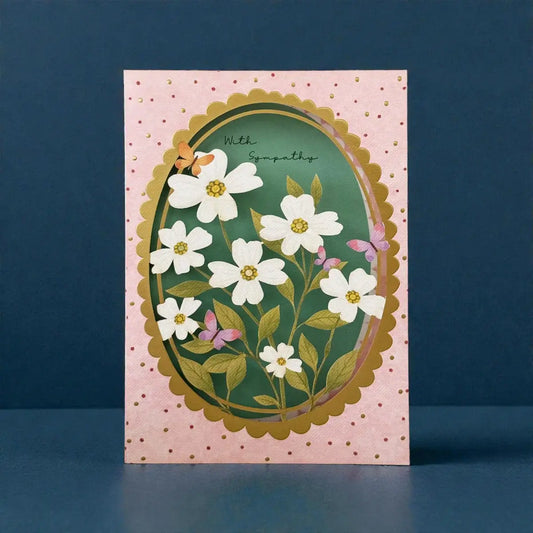 A sympathy card with a pink polka-dot border and a central green oval featuring white flowers, gold scalloped edges, and the handwritten text 'With Sympathy'.