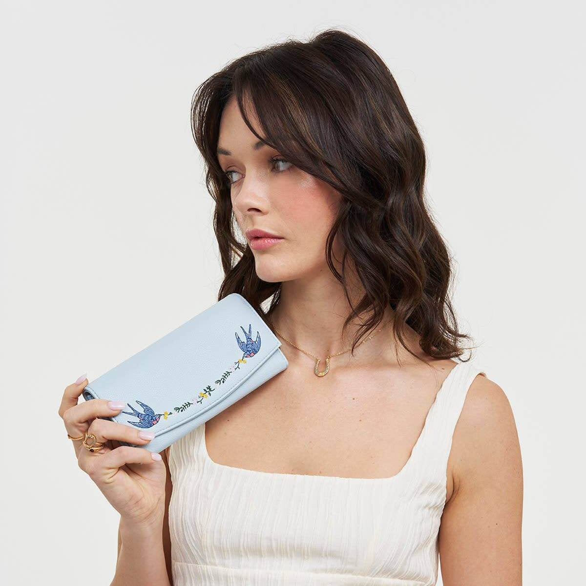 Woman holding a light blue clutch with floral design against a white background