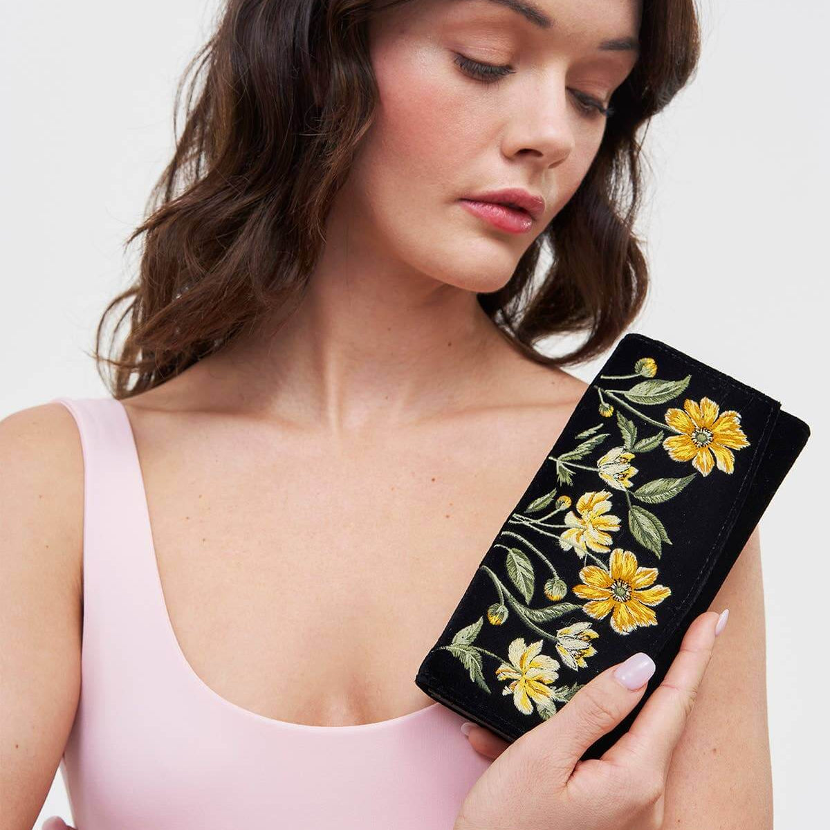 Woman holding a black purse with floral embroidery against a white background