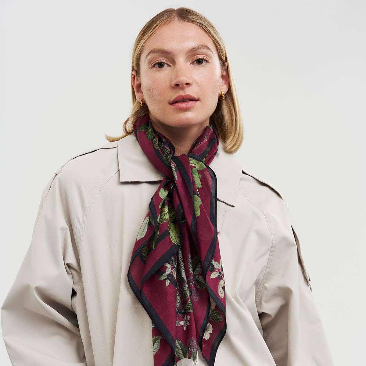 Woman wearing a floral scarf and beige coat on a white background