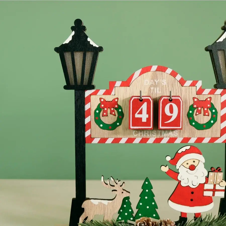 A Christmas advent-style wooden sign with a red-and-white striped arch, three red flip blocks showing 4 and 9, green wreaths with red bows, a Santa Claus figure, a reindeer, and small evergreen trees, photographed against a pale green background.