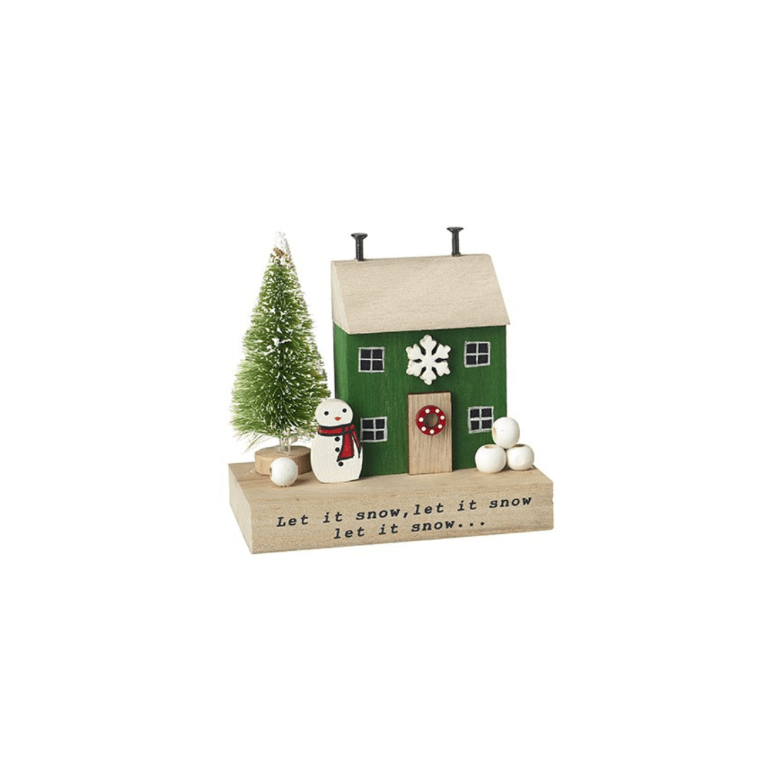 A small Christmas-themed wooden house ornament with a green body, beige roof and base, white snowflake and snowballs, a small green tree, a snowman figure, and printed text reading 'Let it snow, let it snow.