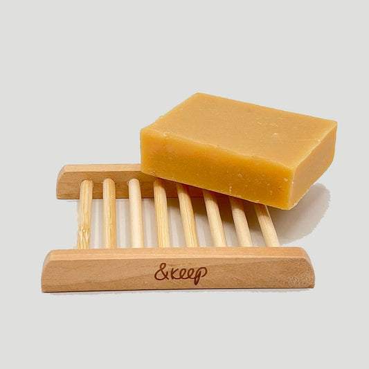 Bar of soap on a wooden soap dish with 'keep' branding on a light gray background
