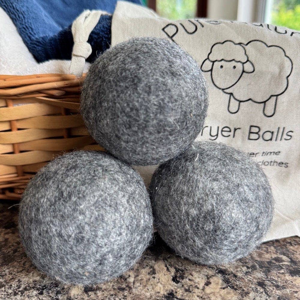 Three grey dryer balls on a countertop with a bag labeled 'Dryer Balls' in the background.