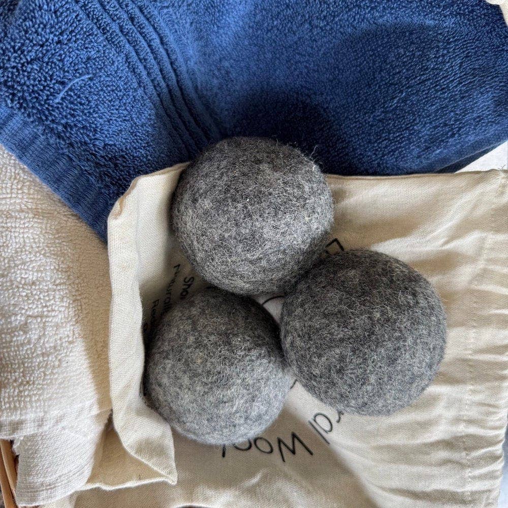 Three gray wool dryer balls on a white fabric background with a blue towel.