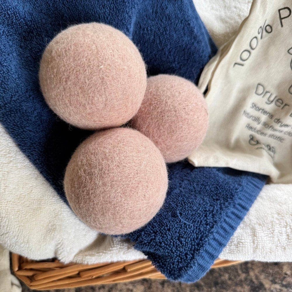 Three pink dryer balls on a blue towel with a bag labeled 'Dryer Balls' in the background.