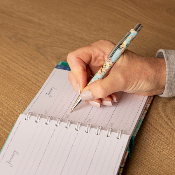 Hand holding a pen over an open planner on a wooden surface