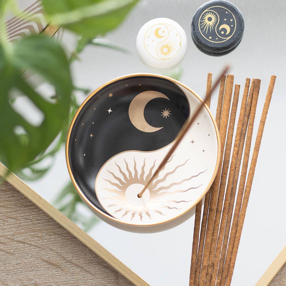 Decorative dish with yin yang design, incense sticks, and a candle on a reflective surface.