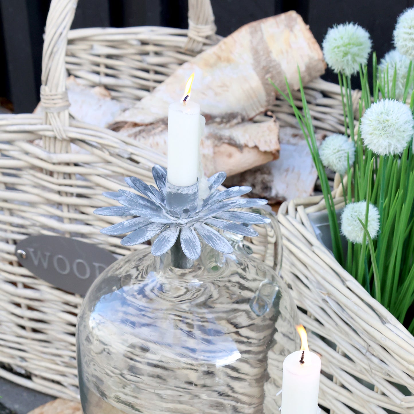 Decorative setting with a glass bottle, candle, and flowers in a wicker basket.