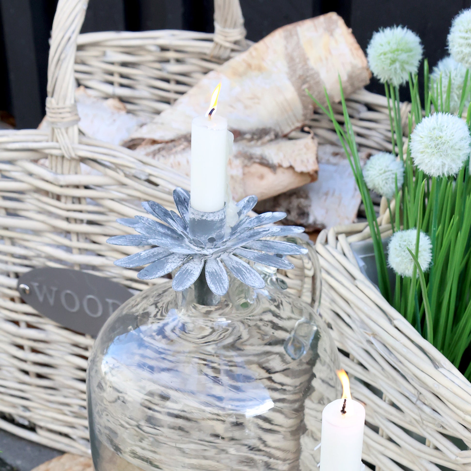 Decorative setting with a glass bottle, candle, and flowers in a wicker basket.