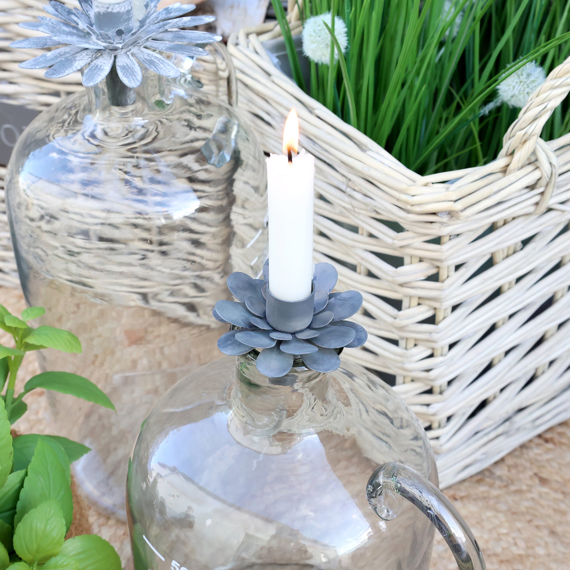 Decorative candle holder with a candle in front of a wicker basket and glass jar.