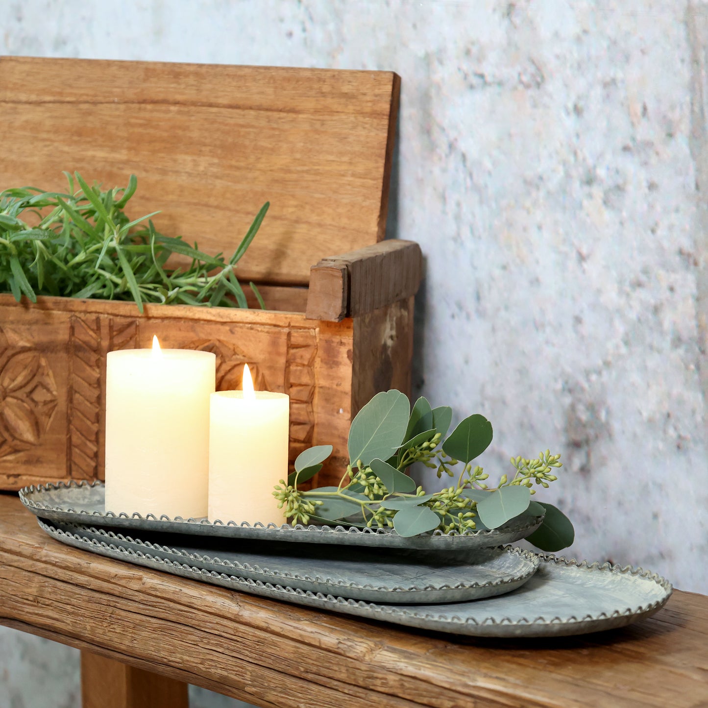 Decorative setting with candles, greenery, and ceramic plates on a wooden surface.