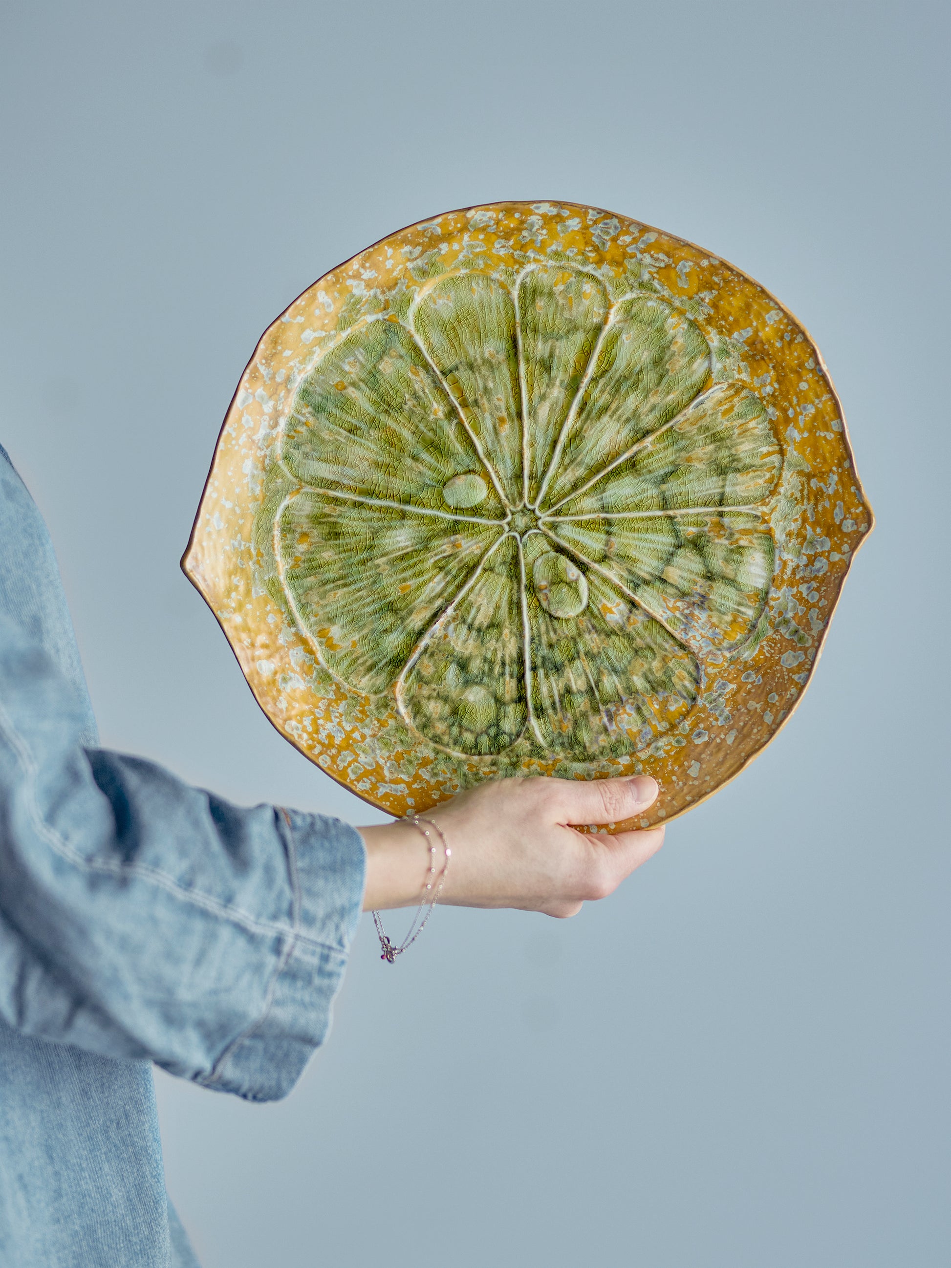 Person holding a decorative ceramic plate with a geometric design against a gray background