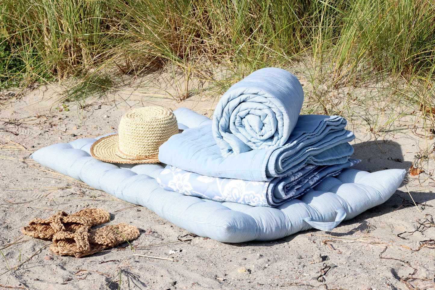 Stack of blue towels on a beach with a straw hat and sandals.