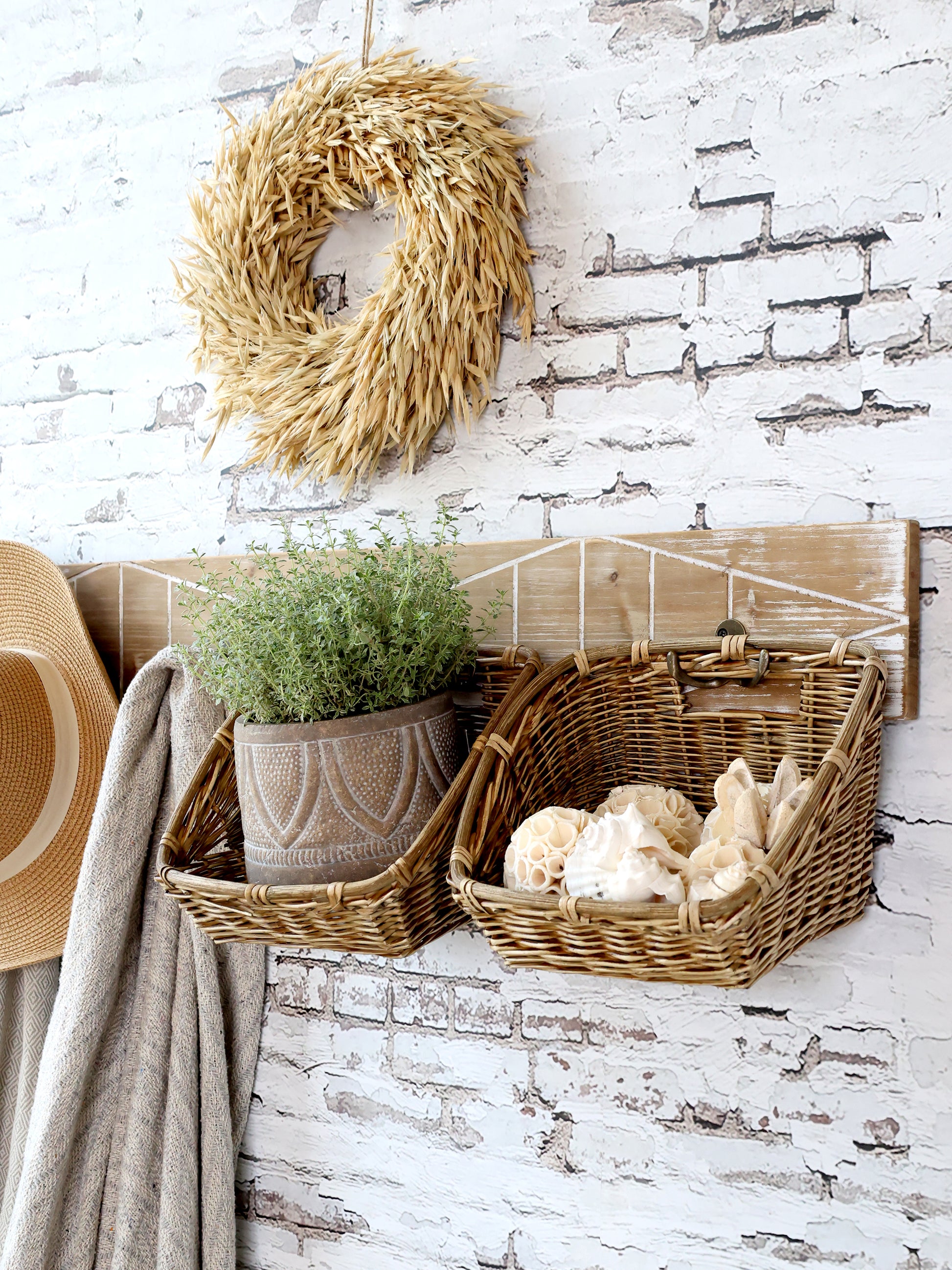 Decorative elements including a straw wreath, baskets with plants and shells, and a hat on a white brick wall.