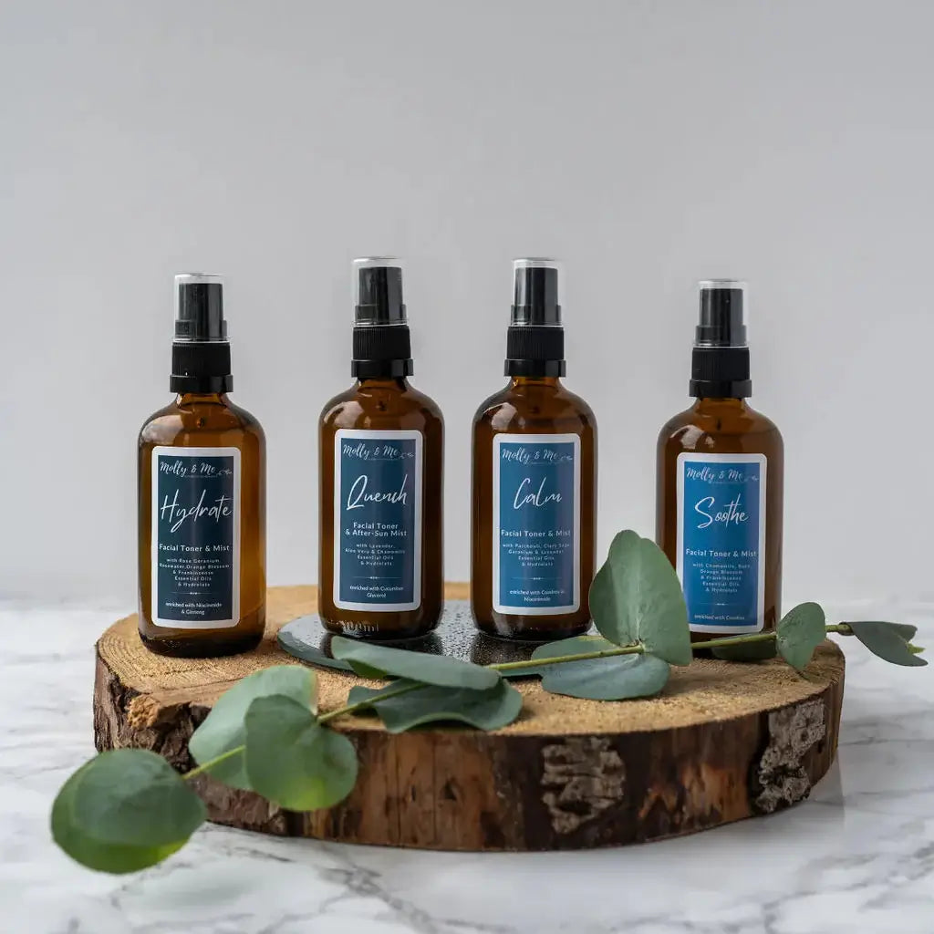 Four brown spray bottles with labels on a wooden block with eucalyptus leaves against a light background